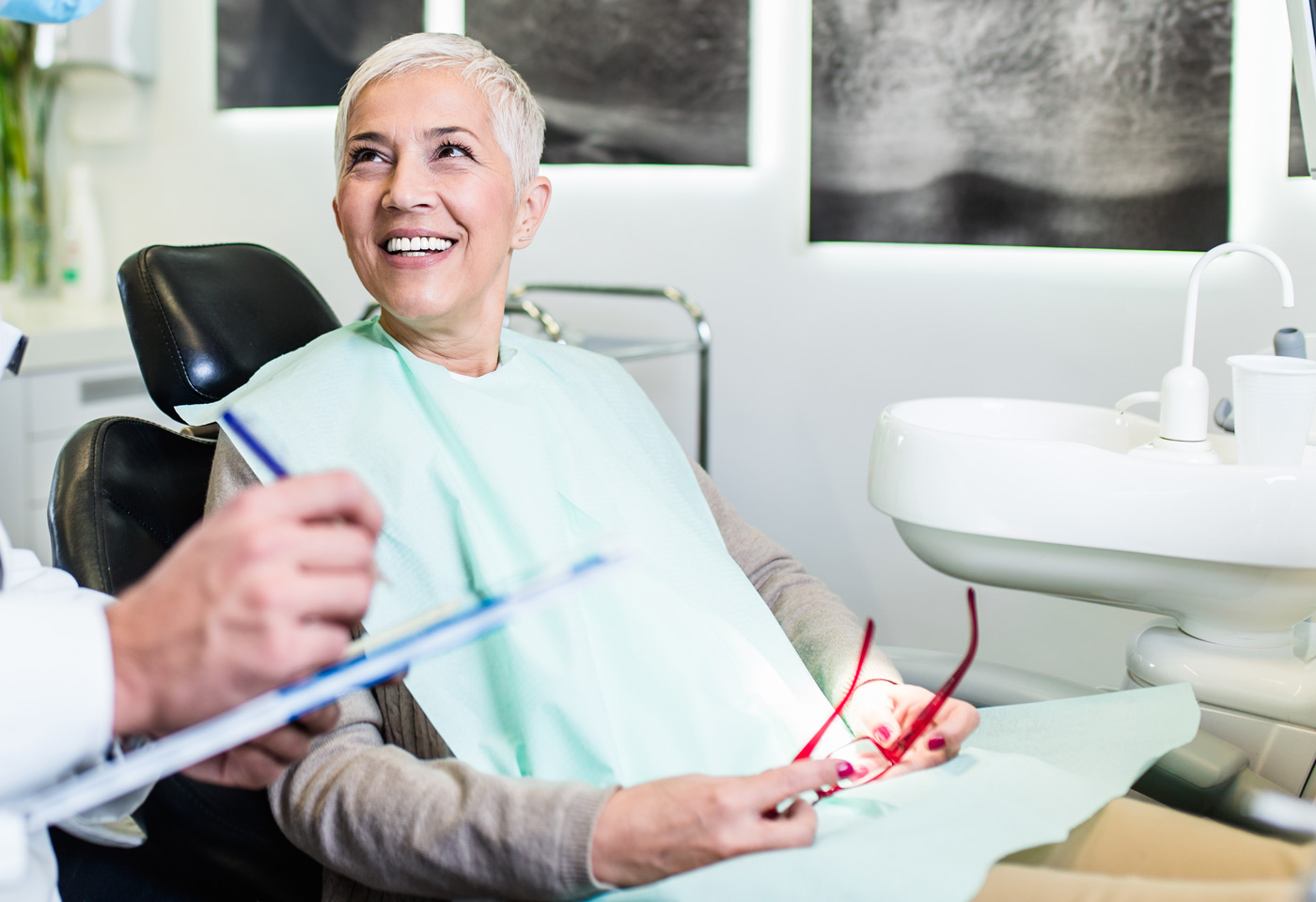 A woman in a dental chair smiles at the dentist, while the dentist explains the root canal procedure.