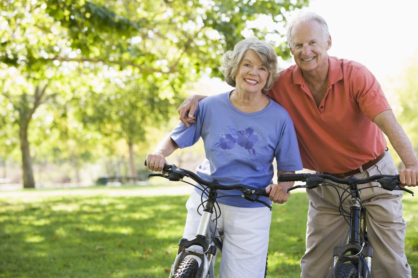 An elderly man and woman each holding a bicycle smiling, showcasing their dental crowns.