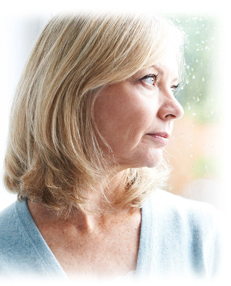 An older woman looking outside the window, reflecting on dental implant procedure.
