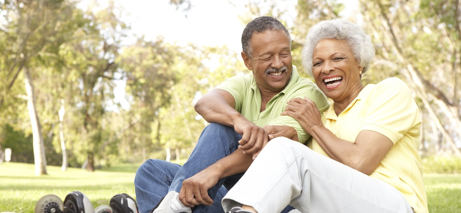 A happy elderly couple sits on the grass, smiling and embracing, portraying a life free from the discomfort of dental issues.