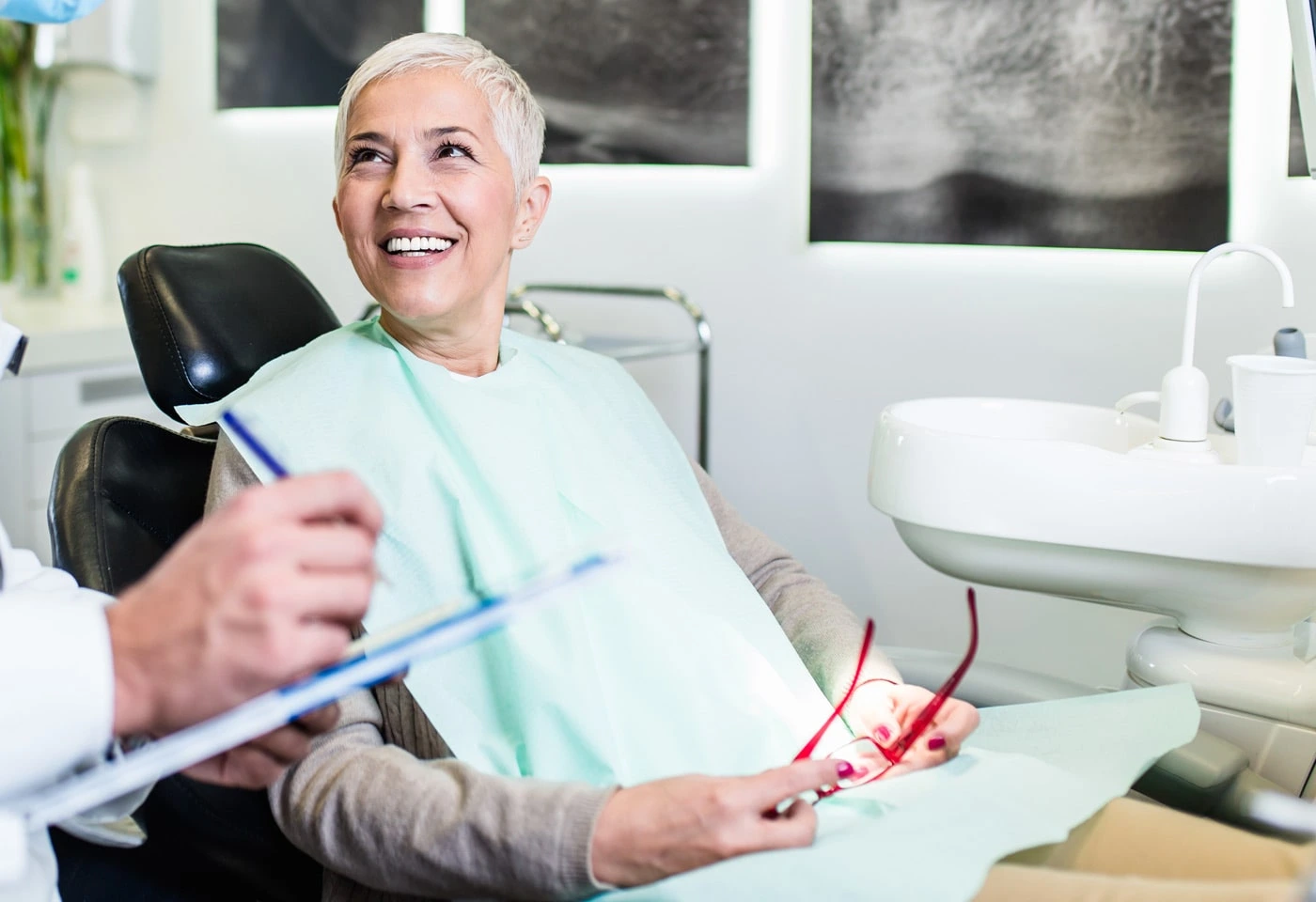 A woman in a dental chair smiles at the dentist, while the dentist explains the root canal procedure.